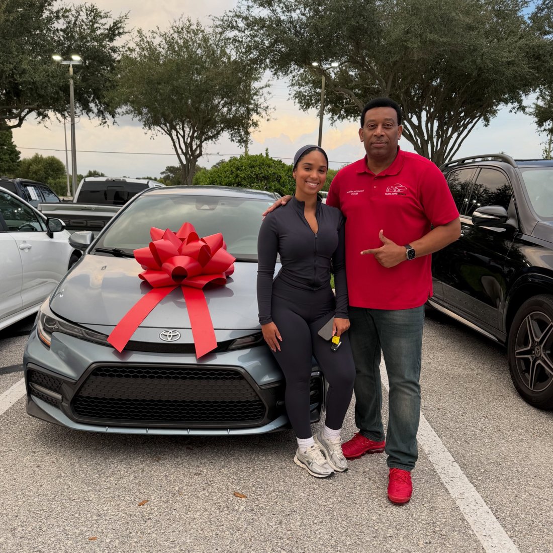 Martindale and a customer beside a Toyota sedan with a red bow
